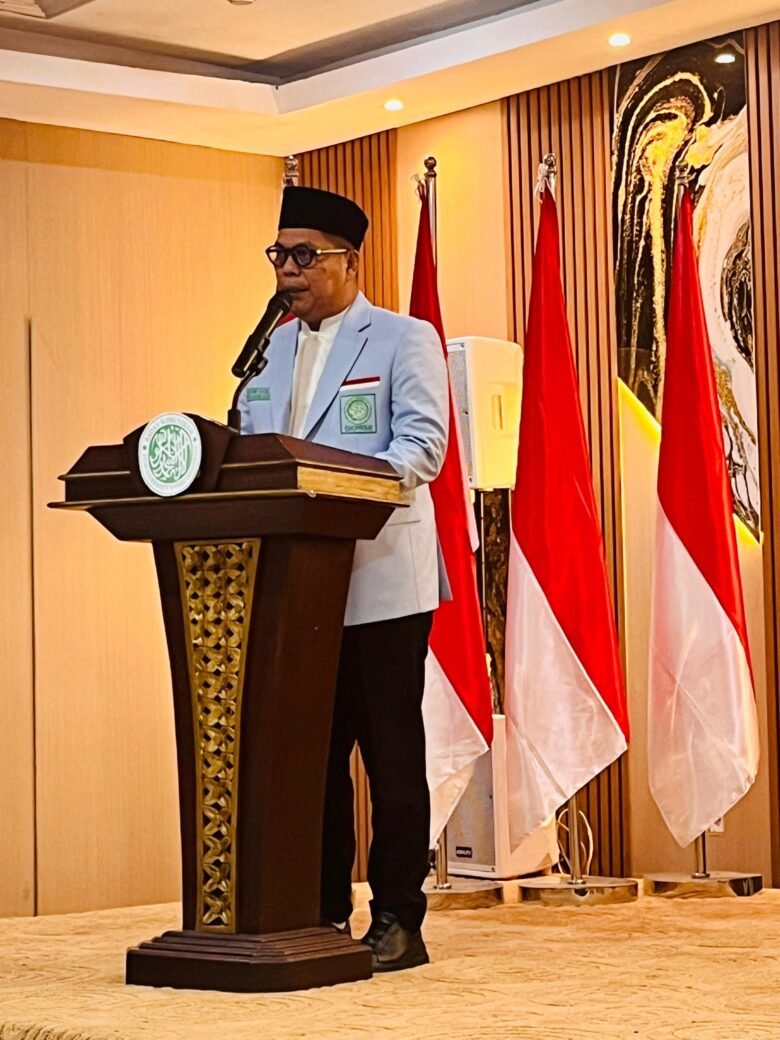 Seorang pembicara berpeci menyampaikan sambutan di podium dalam acara resmi di Banten, dengan latar bendera Merah Putih dan ruang pertemuan formal.